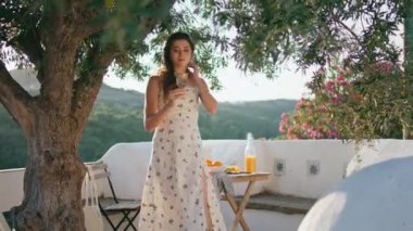 Siesta 'lı kadın terasta su içiyor. Gevşemiş narin kız, ağacın altında limonata yudumluyor ve balkonda tek başına yürüyor. Romantik model panoramik mekanda soğuk sıvı içecekten keyif alıyor.