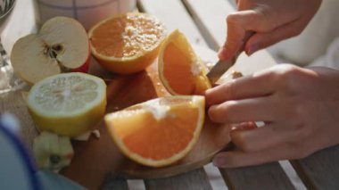 Kapalı kadın elleri yaz balkonunda tahta tahtada turuncu kesiyor. Anonim bir kadın elinde bıçakla Sunshine Terrace 'da meyve doğruyor. Tanımlanamayan model açık havada kahvaltı hazırlıyor.