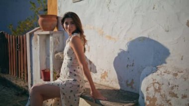 Seksi kadın, güneş gören köy bankı. Gülümseyen romantik kadın saçlarına dokunuyor yaz ortasında eski Beyaz Saray duvarına yaslanıyor. Güzel esmer, ısınan güneş ışınları tatilde hafif rüzgarın tadını çıkarıyor.