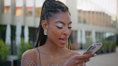 Modern şehir binasının önünde konuşan Afro-Amerikan modacı telefon mikrofonu. Moda görünümlü kadın cep telefonu asistanı uygulaması kullanarak sesli mesaj kaydediyor. Hoparlörden konuşan şık bir kız.