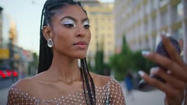 Gülümseyen kadın Urban Bulvarı 'nda aynaya bakıp makyaj yapıyor. Afrika kökenli Amerikalı moda tutkunu küpelere dokunuyor ve yaz akşamı sokağına bakıyor. Moda insan yaşam tarzı konsepti