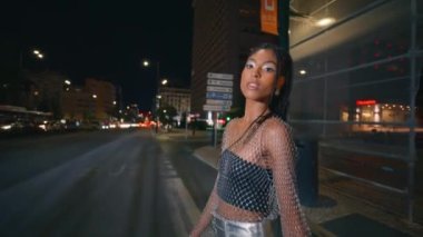 Koyu tenli manken yalnız başına gece gezintisi yapıyor. Afro örgülü kadın trafik sıkışıklığı yolundan geçip kamera görüntüsü çiziyor. Moda görünümlü kadın elini uzatıp gezintiden zevk alıyor. Şık insanlar yaşam tarzı.