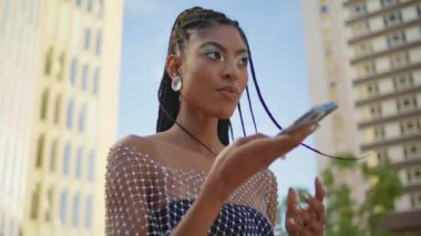 Yaz sokağı kapanışında konuşan modaya uygun bir kadın. Afro-Amerikan bayan akıllı telefon mikrofonundan cep telefonu asistanı uygulaması kullanarak sesli mesaj kaydediyor. Modern teknoloji kavramı 