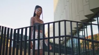 Modern bina şehrinde merdivenlerden inen şık bir model. Dreadlocks çekici Afrikalı Amerikalı kadın merdivenlerde yalnız başına sakin bir şekilde dolaşmaktan hoşlanıyor. Aktif modaya uygun esmer aşağıya inip şehri keşfediyor.