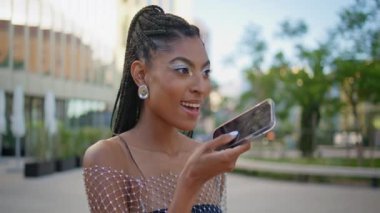 Şık bir kadın sokak kapanışında akıllı telefon mikrofonundan sesli mesaj kaydediyor. Cep telefonu uygulaması kullanarak hoparlörden konuşan mutlu Afro-Amerikan bayan. Modern teknoloji kavramı 