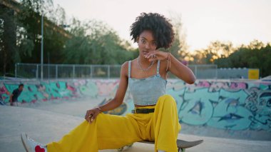 Modern buz pateni parkında kaykay yapan havalı bir hippi. Güzel Afrikalı Amerikalı kız kaykay seyrediyor. Popüler kıvırcık genç kaykaycı sokakta poz vermenin keyfini çıkar..