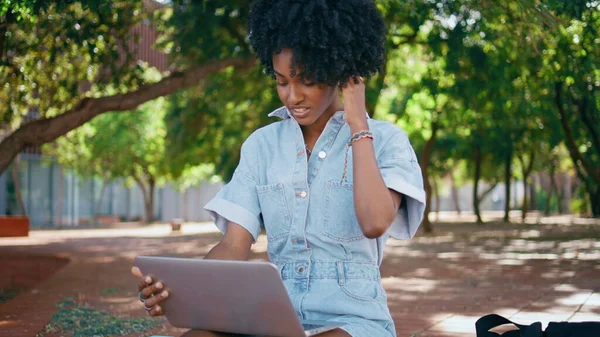 African girl video calling looking laptop web camera sitting green park closeup. Smiling beautiful woman in headphones talking at online meeting outdoors. Happy student chatting by internet connection