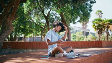Moda kızı akıllı telefondan selfie çekiyor sokak ağaçlarının altında oturuyor. Güzel afro-amerikan genci fotoğrafçılık yapıyor. Tasasız gençler ders çalıştıktan sonra parkta cep telefonuyla rahatlarlar..