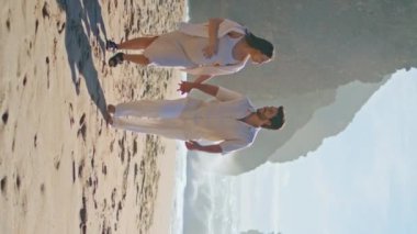 Hamile çift güzel yaz tatilini dikey olarak sahilde yürüyor. Mutlu genç çift öpüşmek için durup güneşli deniz kıyısında dinleniyor. Sevgi dolu eşler bebek bekliyor Romantik tatilde sevinç hissediyorlar.