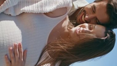 Hamile bir aile kumsalda dinleniyor, göbeğini okşuyor, dikey olarak ona yakın duruyor. Sevgili eşimin arkasında durup karnını kucaklayan mutlu bir koca. Deniz kenarında hamileliğin tadını çıkaran hassas bir çift.
