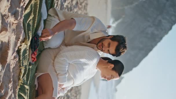 期待的父母喜欢在沙滩上野餐 夏夜的垂直天使 照看小孩的男人看着海浪 用浆果喂怀孕的妻子 未来的父亲母亲抱着孩子躺在毛毯上 — 图库视频影像