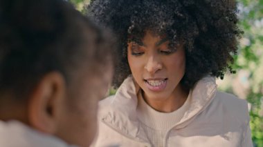 Neşeli anne parktaki küçük şirin kıza dokunuyor. Yaklaş. Gülümseyen Afro-Amerikan kadın. Güneşli doğada tatlı kız parmaklarıyla oynuyor. Yeşil ormanda tasasız aile hafta sonu.