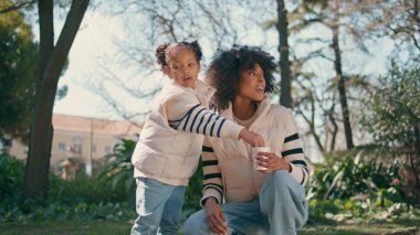 Yeşil parkta annesi ile duran kuşlara ekmek kırıntıları atan sevimli bir çocuk. Küçük Afrikalı Amerikalı kız annesinin elinden güvercin maması alıyor. Sevimli güzel çocuk güvercinleri dışarıda beslemeyi sever..