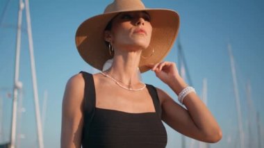 Hasır şapkalı kız güneşli doğada dinleniyor. Yaklaş. Yaz tatilinde yelken direğinde poz veren zarif bronzlaşmış kadın portresi. Lüks başlıklı moda manken rıhtımda duruyor..