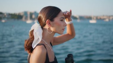 Turist kadın güzel okyanus kıyısına dürbünle bakıyor. Yakından. Güzel esmer kız gülümseyip güneşli deniz manzarasını seyrediyor. Zarif saç stili ve deniz manzaralı çekici bir bayan..