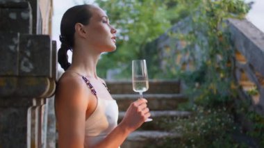 Eski şatonun merdivenlerinde şarap kadehi tutan şık bir kadın. Ortaçağ sarayında tek başına kameraya bakan zarif bir bayan. Muhteşem kız eski duvarlara yaslanmış lezzetli alkolün tadını çıkarıyor.