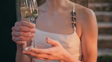Kadın elleri dışarıda rafine alkollü şarap bardağını tutuyor. Seçkin cam kadehteki beyaz şaraba bakan tanınmamış bir kadın. Meçhul kız şampanyayla serin partinin tadını çıkar.
