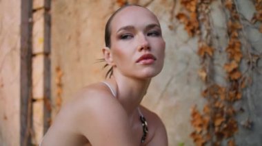 Eski duvarın önünde güneş ışığında poz veren manken kuru yaprakları kapatıyor. Terk edilmiş bir yerde oturan mükemmel ciltli, kendine güvenen güzel bir kadının portresi. Ciddi bayan dışarıda dinlenmeyi sever.