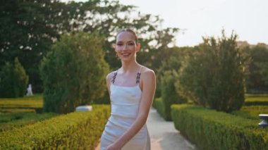 Gülümseyen kadın yeşillikte geziniyor ve güzel yaz manzarasının tadını çıkarıyor. Zarif beyaz elbiseli, kaygısız kız park yolunda yürüyor. Göz kamaştırıcı, neşe dolu bir kadın Resimli, bereketli bahçede dinleniyor.