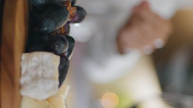 Ahşap pano restoran masasında dikey olarak duran kırmızı şaraba lezzetli aperatifler. Erkek eli alkolle tatmak için üzüm alıyor. Meçhul çeşnicibaşı merlot ile peynir tahtasını seviyor
