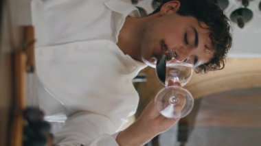 Tecrübeli şarap uzmanı ahşap masadaki lüks restoranda kırmızı şarap tadıyor ve aperatifler dikey olarak yakın planda. Kendine güvenen İtalyan şarap garsonu üzümlü alkolün tadını kontrol ediyor.
