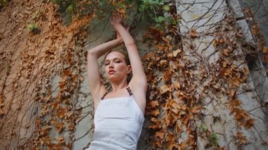 Çekici bir model terk edilmiş eski binada el kaldırıyor. Duvara yaslanan muhteşem seksi kadın doğadaki sonbahar yapraklarını kaplamış. Şehvetli zarif kız kameraya bakıyor. Dışarıda sakinlik hissediyor..
