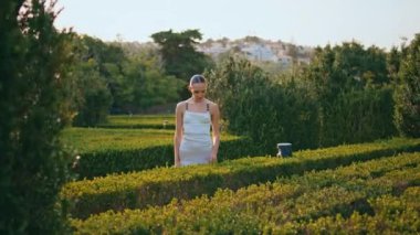 Güzel yeşil parktaki çalılara dokunan hayalperest kadın. Romantik, rahat bir kız, hafta sonu bahçede çitin tadını çıkarıyor. Yeşillik içinde doğada poz veren muhteşem bir bayan model..