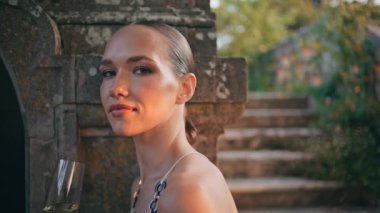 Ortaçağ Şatosu 'nda cam kadehte şampanya içen muhteşem bir kadın. Tasasız genç bir kadın, elinde beyaz şarapla terk edilmiş eski sarayda dinleniyor. Güzel kız merdivenlerde kameraya bakıyor.