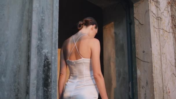 ファッションの女性は 石のアーチを歩く中世の城を楽しんでいます 見捨てられた宮殿に入るカメラを見つめている少女は 日光を浴びる 古い壁に触れるトレンディなドレスの深刻な官能的なモデル — ストック動画