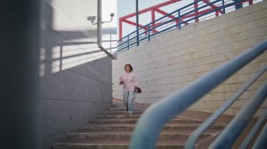 Kız kaykaycı elinde modern bir sörf tahtasıyla merdivenlerden aşağı iniyor. Kaykaylı rahat genç bir kadın merdiven kentinde müzik dinliyor. Kaygısız genç kız gezerken kulaklık takıyor..