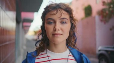 Portre kulaklıklı kız hafta sonu şehir merkezinde kameraya bakıyor. Kulaklıkla müzik dinleyen tatlı kıvırcık ergen şehir caddesinde duruyor. Gülümseyen moda kadın kulaklıkla dışarıda poz veriyor.