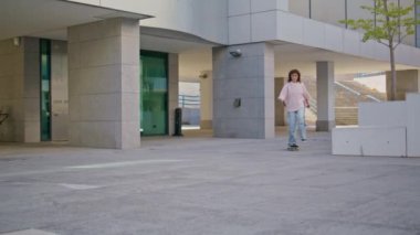 Kentsel caddede kaykay süren rahat bir kız. Modern şehir bölgesinde kaykay yapan genç ve kaygısız bir kadın klasik bir oyuncunun müziğini dinliyor. Güzel bayan genç açık havada spor yapmayı seviyor..