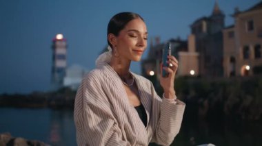 Havalı iş kadını deniz kenarındaki alacakaranlıktan arıyor. Gülümseyen mutlu bir kadın, akıllı telefonlardan bahsederek akşam sahil şehrinde oturuyor. Güzel kız gülümsüyor, arkadaşça telefon konuşmalarının tadını çıkarıyor..