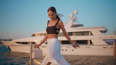 Rıhtımda poz veren modacı kız kameraya kendinden emin bakıyor. Beyaz yatın önünde duran lüks bir genç kadın. Gülümseyen zarif bayan turist yaz tatilinde deniz kenarında dinleniyor.