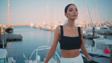 Rıhtımda modaya uygun kıyafetlerle poz veren kendinden emin bir kadın. Beyaz yatların önünde setin önünde duran zarif, lüks bir kız. Akşam rıhtımında poz veren zengin genç bayan. Muhteşem bayan turist.