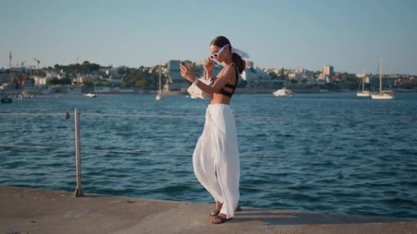 快乐的女孩在海洋码头流口水使用智能手机 迷人的时髦女人在堤岸上为社交媒体录制视频制作内容 看着站在海面上的移动相机的豪华型 — 图库视频影像