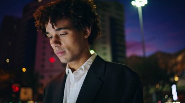 Mutlu iş adamı yalnız başına gece gezintisine çıkıyor. Kıvırcık saçlı bir çalışan akşam gezintisi portresinin keyfini çıkarıyor. Aydınlanmış iş bölgesinde sakince hareket eden rahat genç bir adam. Latin adam aşağı bakıyor.