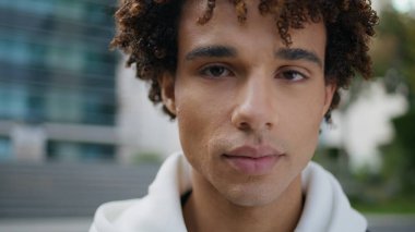 Kıvırcık suratlı, poz veren şehir resmi. İş bölgesinde kameraya bakan genç adam yakın çekim yapıyor. Caddede gülümseyen latin model gözlük. Kentsel arka planda neşeli genç ifadesi 