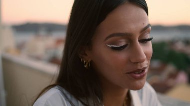 Gülen kadın balkon portresi konuşuyor. Esmer kadın yüzü, günbatımında deniz oteli randevusunda konuşuyor. Yakından gülümseyen kız romantik yemek terasında sohbet ediyor. Latin insan sohbeti. Hayat rahatlatıcı zaman