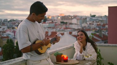 Sunset City Manzara Terası 'nda gitar çalan yakışıklı adam. Romantik bir buluşmada birlikte müzik dinleyen sevgi dolu bir çift. Koca, karısına ukulele şarkıları söylüyor. Şefkatli sevgililer balayının tadını çıkarıyor