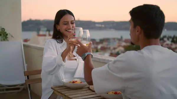 Young lovers toasting hotel at sunset closeup. Smiling woman having romantic dinner with man. Relaxed pair drinking wine glass celebrating honeymoon. Cheerful spouses sitting terrace enjoying view