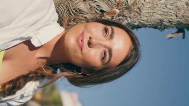 Gevşek model güneş ışınları arka sokakta dikey olarak yakınlaşıyor. Güneşli doğada gülümseyen mutlu gezgin kız tropikal ağaç ortamında dinleniyor. Neşeli kadın tatilin tadını çıkarıyor. Hafta sonu etkinliği