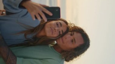 Neşeli gençler gün batımında plajın dikey meleğinde selfie çekiyorlar. Mutlu sevgililer cep telefonlarının fotoğraflarını çekiyor akşam doğasında kucaklaşıyorlar. Deniz kıyısında bir kadını öpen aşık bir genç adam.
