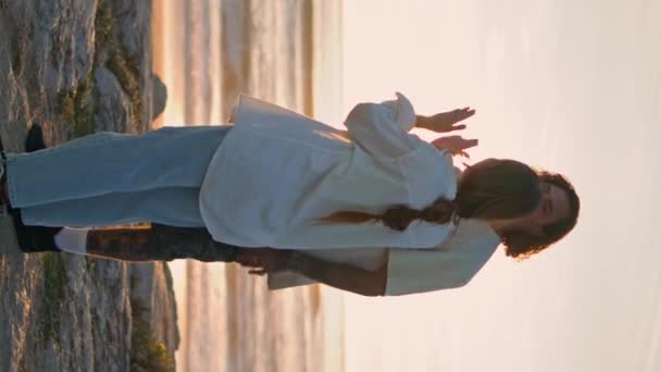 一对快乐的伴侣在夕阳西下的海面上玩耍狗 年轻人在晚上把岩石扔到海里拥抱可爱的女朋友 喜欢沙滩上的青少年 在海岸线上奔跑的小狗 — 图库视频影像