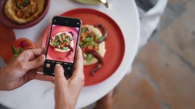 Kadın eli restoran masasında cep telefonuyla lezzetli bir yemeğin fotoğrafını çekiyor. Kimliği belirsiz kişi dijital akıllı telefon pov 'unda fotoğraf çekiyor. Müşteri kafede yemeğin tadını çıkarıyor. Öğle yemeği konsepti