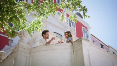 Sokağın balkonunda kadeh kaldıran romantik sevgililer. Mutlu çift, gün ışığı şehrinde kadeh tokuşturarak içki içiyor. Aşık, neşeli bir kadın üzüm suyu içiyor.