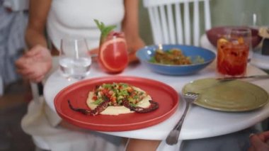 Pahalı bir kafede el ele tutuşan bir kadın. Arkadaşlarıyla buluşurken ahtapot dokunaçlarıyla humusun tadını çıkaran tanınmamış bir kadın. Meçhul kızlar yemek tadıyor.