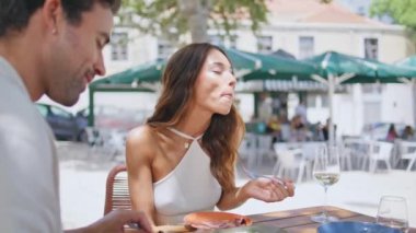 Caddedeki kafede kocasıyla yemek yiyen aç bir kız. Rahatlamış lüks aşıklar birlikte restoran terasında yemek yiyorlar. Çatal tutan esmer, gülümseyen kadın lezzetli yemekler yiyor.