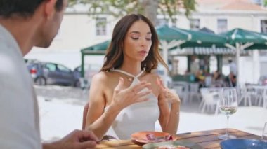 Duygusal bir kadın sokak kafesinde el hareketleriyle yemek yiyor. Restoran terasında öğle yemeği yiyen rahat ve zarif bir çift. Esmer kadın erkek arkadaşıyla konuşuyor, yemek tadıyor.
