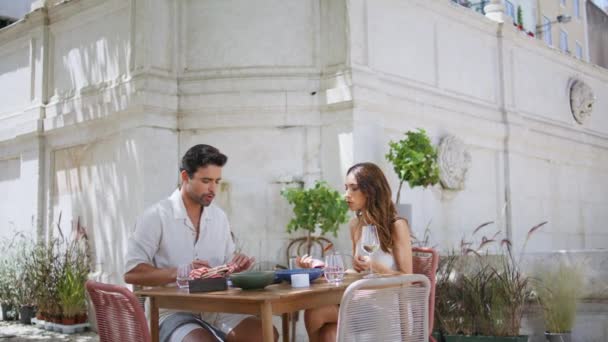 微笑的情人在城市餐桌边聊天 迷人的夫妻喜欢在街上的咖啡馆里约会 两个年轻人在谈论户外品食的新闻 舞伴们在院子里玩得很开心 — 图库视频影像